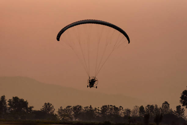 istock Silhouette of the Paramotor gliding and flying In the air through soft sunlight sky. 1323042000