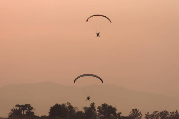 istock Silhouette of the Paramotor gliding and flying In the air through soft sunlight sky. 1323042011