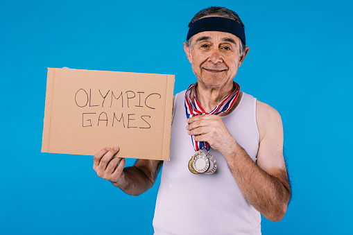Elderly athlete with sun marks on his arms, with three medals around his neck and a sign that reads: \