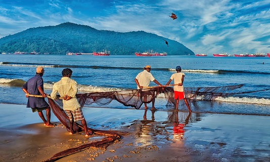 Karwar, Karnataka India - September 15 2018: A group of local fishermen at seashore pulling nets from the sea. Fishermen face a tough job but this is the way they earn their living. selective focus.