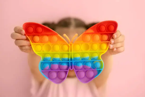 Photo of The girl is holding a bright colorful popit toy in the shape of a butterfly