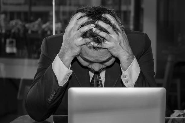 An Asian male businessman is sad and crying in front of the computer laptop for his failure management in finance business investigation work and job during a strong economic crisis issue stock photo