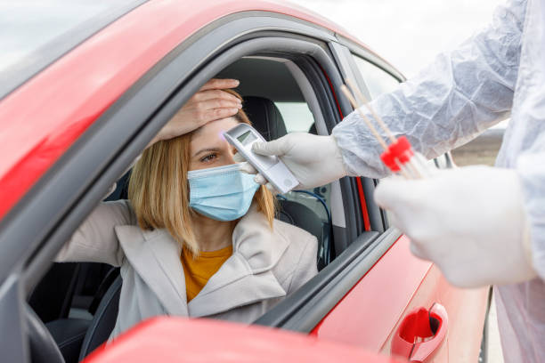 istock Medic using hand held infrared thermometer for a woman driving a car 1323066079