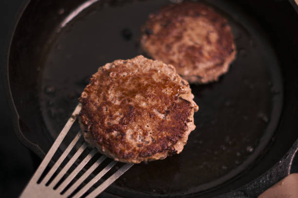 Well crusted hamburger patties sizzling in a cast iron skillet.