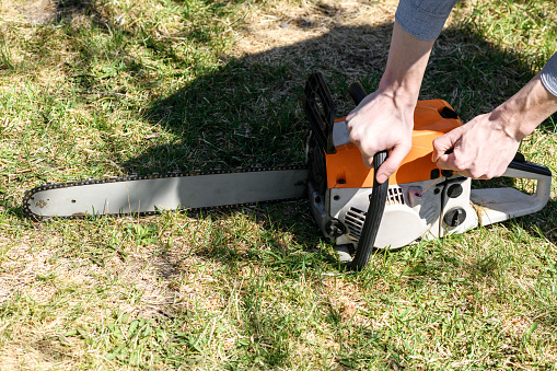 A man starts a chainsaw, top view on the green grass on a sunny day. Concept is to cut trees