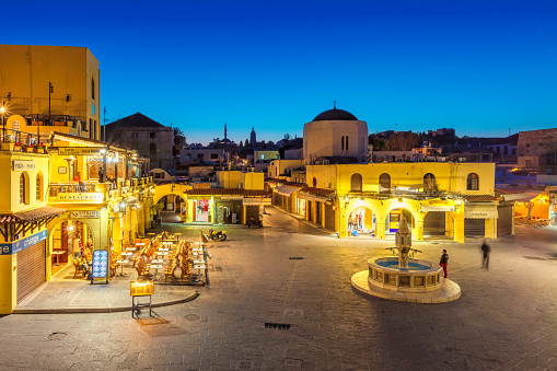 People relax on Hippocrates Square in downtown Rhodes, Greece at twilight.