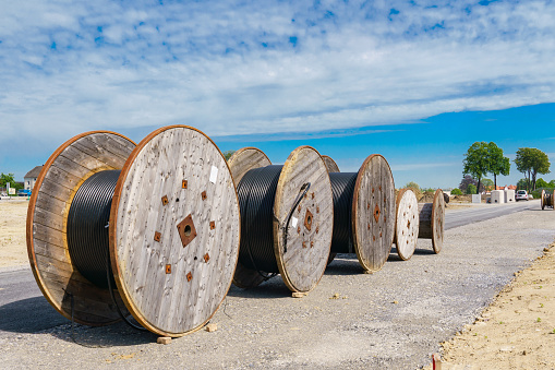Wooden spools of cables are lined up at a construction site. Clear sunny day.