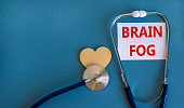 Medical, covid-19 and brain fog symbol. White card with words 'brain fog' and stethoscope on blue background. Wooden heart. Medical, covid-19 brain fog concept. Copy space.