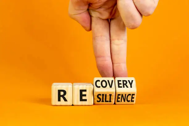 Photo of Recovery and resilience symbol. Businessman turns cubes and changes the word 'recovery' to 'resilience'. Beautiful orange background. Business and recovery - resilience concept. Copy space.