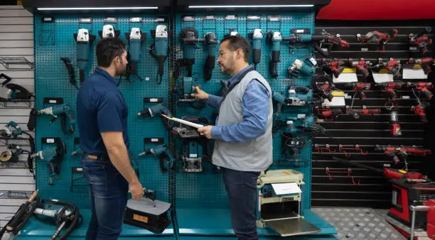 Latin American customer shopping for tools at a hardwarestore and talking to a salesman - small business concepts