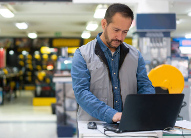 Salesman working at a hardware store and checking the stock on a laptop