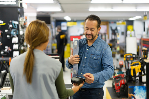 Latin American man making a contactless payment at a hardware store while buying some tools - small business concepts