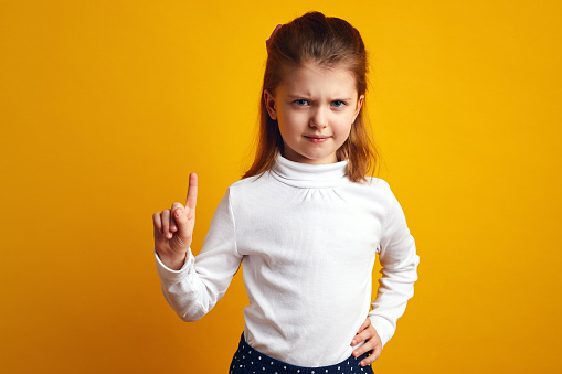Displeased young girl waving index finger in no and prohibition gesture making mad face holding hand on waist, giving advice to stop