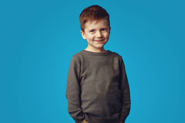 istock Kid smiling while holding hands in pockets, isolated over blue background 1323087130