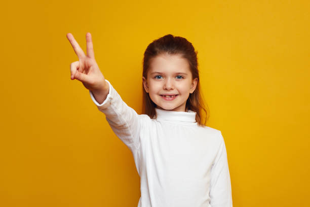 istock Optimistic girl kid showing peace gesture against bright yellow background 1323087132