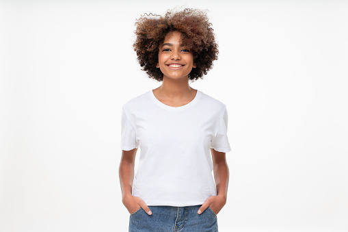Front view of african american girl standing with hands in pockets, wearing blank t-shirt with copy space, isolated on white background