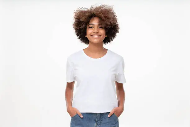 Photo of Front view of african american girl standing with hands in pockets, wearing blank t-shirt with copy space, isolated on white background