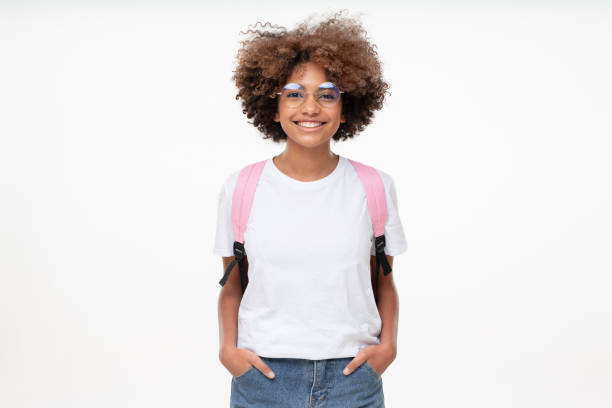 portrait d’une écolière africaine souriante portant un t-shirt blanc, des lunettes et un sac à dos, isolée sur fond gris - schoolgirl photos et images de collection