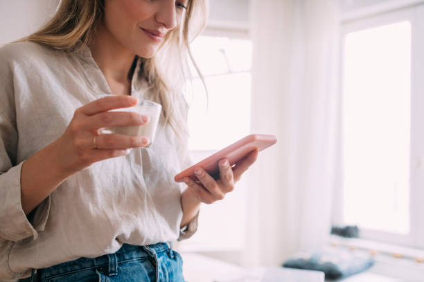 istock Cheerful Woman Drinking Coffee and Using Mobile Phone at Home 1323098109