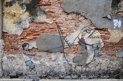 Penang, Malaysia- Dec 27, 2016:  Street art titled Little Boy with Pet Dinosaur by Ernest Zacharevic in Penang, Malaysia.