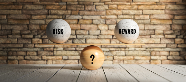 wooden scale balancing spheres with the message RISK, REWARD and ? in front of a brick wall background - 3d illustration