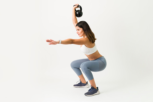 Squats exercises with a kettlebell. Strong caucasian woman squatting while holding a kettlebell weight to workout her arms, legs and back