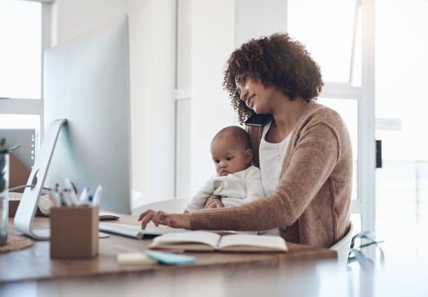 foto de una joven usando un teléfono inteligente y una computadora mientras cuida a su adorable niña en casa - working mother working mother balance fotografías e imágenes de stock