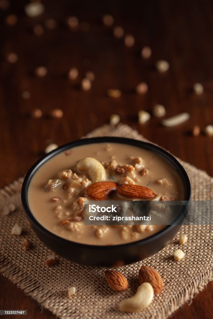 Close up of a famous Bengali dessert "Nolen Gurer Chanar Payesh" or Milk pudding of cottage cheese in a black bowl. Top-down view, wooden background. Kheer Stock Photo