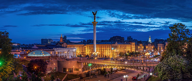 View of the Maidan Nezalezhnosti against the background of the sunset sky with people resting near the illuminated fountains and the Monument of Independence of Ukraine.