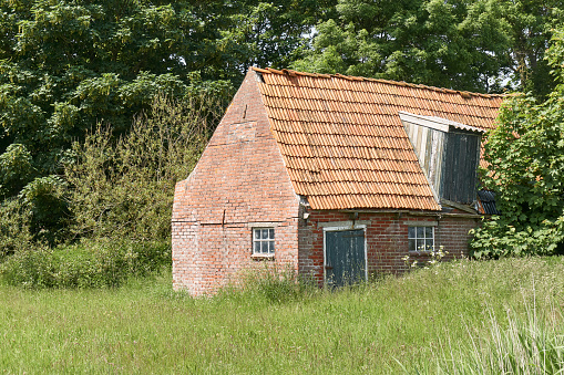 Old decaying shed with red bricks and orange tiles near Ferwerd in The Netherlands.