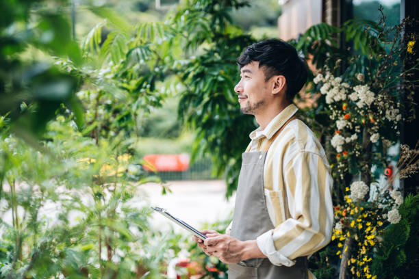 portrait of confident young asian male florist, owner of small business flower shop, standing in front of flower shop, smiling and planning the next step in his business. small business concept - aspirations growth expressing positivity selling imagens e fotografias de stock