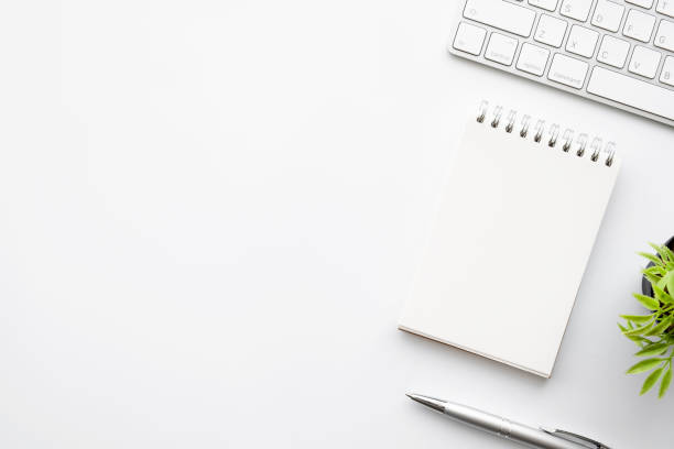 istock Blank notebook is on top of white office desk table with pen. Top view with copy space, flat lay. 1323146562