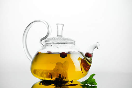 Yellow herbal tea in glass teapot and cup with leaves and berries. Close-up   freshly brewed hot tea.