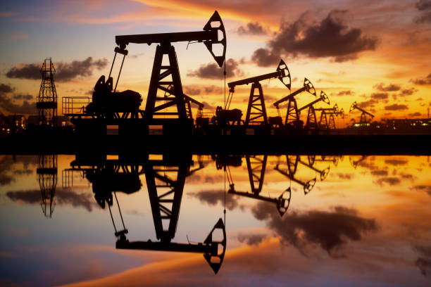 Oil Pumps And Rig At Sunset By The Sea Pump jack silhouette against a sunset sky with reflections in the water. north sea oil and gas stock pictures, royalty-free photos & images