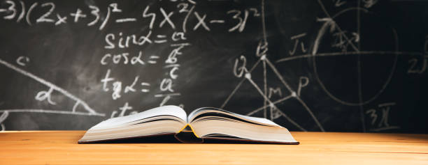 istock Open book on the table in classroom with blackboard background 1323157470