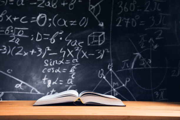 istock Open book on the table in classroom with blackboard background 1323157513