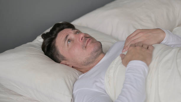 istock Pensive Middle Aged Man Laying Awake in Bed 1323158741