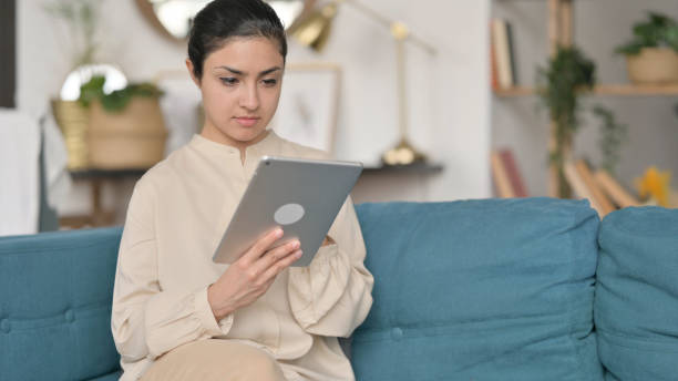 istock Young  Indian Woman using Tablet on Sofa 1323160709