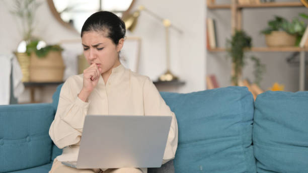 istock Young Indian Woman with Laptop Coughing  on Sofa 1323161143