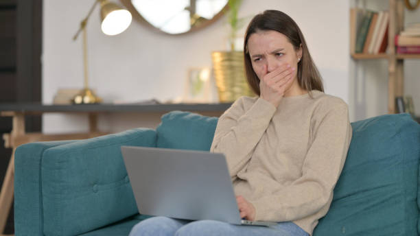 istock Young Woman with Laptop Coughing  on Sofa 1323161926
