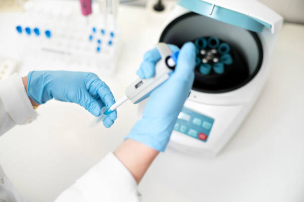 researcher using pipette and analysis flask samples into a centrifuge in laboratory. Woman researcher is placing test tubes in the special machine.