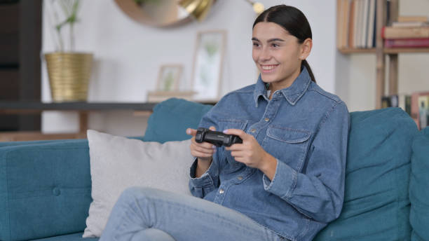 istock Attractive Latin Woman Playing Video Game on Sofa 1323162084
