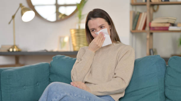 istock Sick Young Woman Sneezing Sitting on Sofa 1323162115