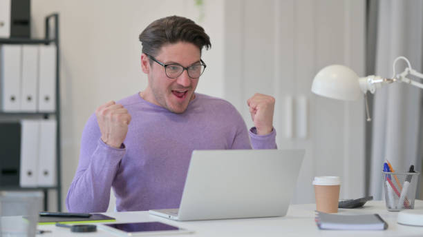 istock Middle Aged Man with Laptop Celebrating in Office 1323162210