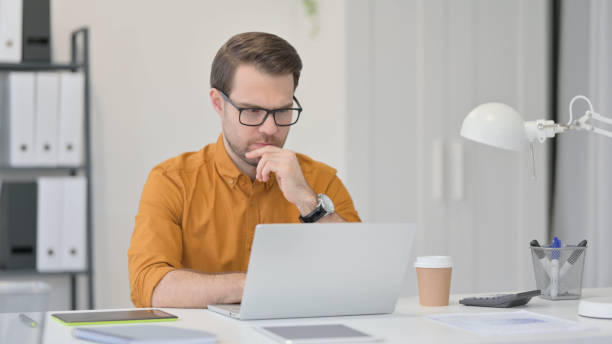 istock Young Man with Laptop, Thinking in Office 1323163182