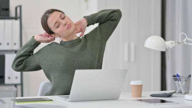 istock Young Woman with Laptop Stretching in Office 1323163484