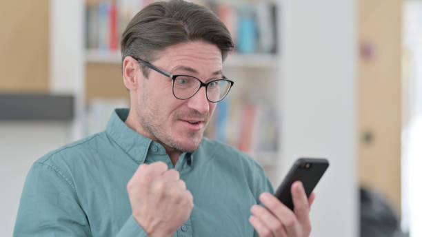 istock Middle Aged Man Excited by Success on Smartphone 1323164426