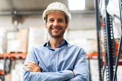 Portrait of happy mature warehouse supervisor wearing hardhat. Warehouse foreman looking at camera and smiling.