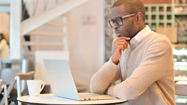 istock Pensive African Man Thinking and Working on Laptop in Cafe 1323166110