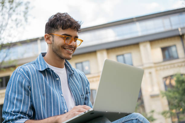 szczęśliwy indyjski programista za pomocą laptopa, internetu, pracy freelance projektu online, siedząc w parku. azjatyccy studenci studiujący, uczący się języka, wykorzystujący nowoczesne technologie na zewnątrz - computer programmer designer computer computer language zdjęcia i obrazy z banku zdjęć